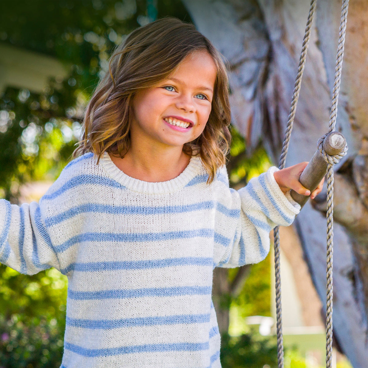Young girl in a striped sweater on a swing with trees in the background