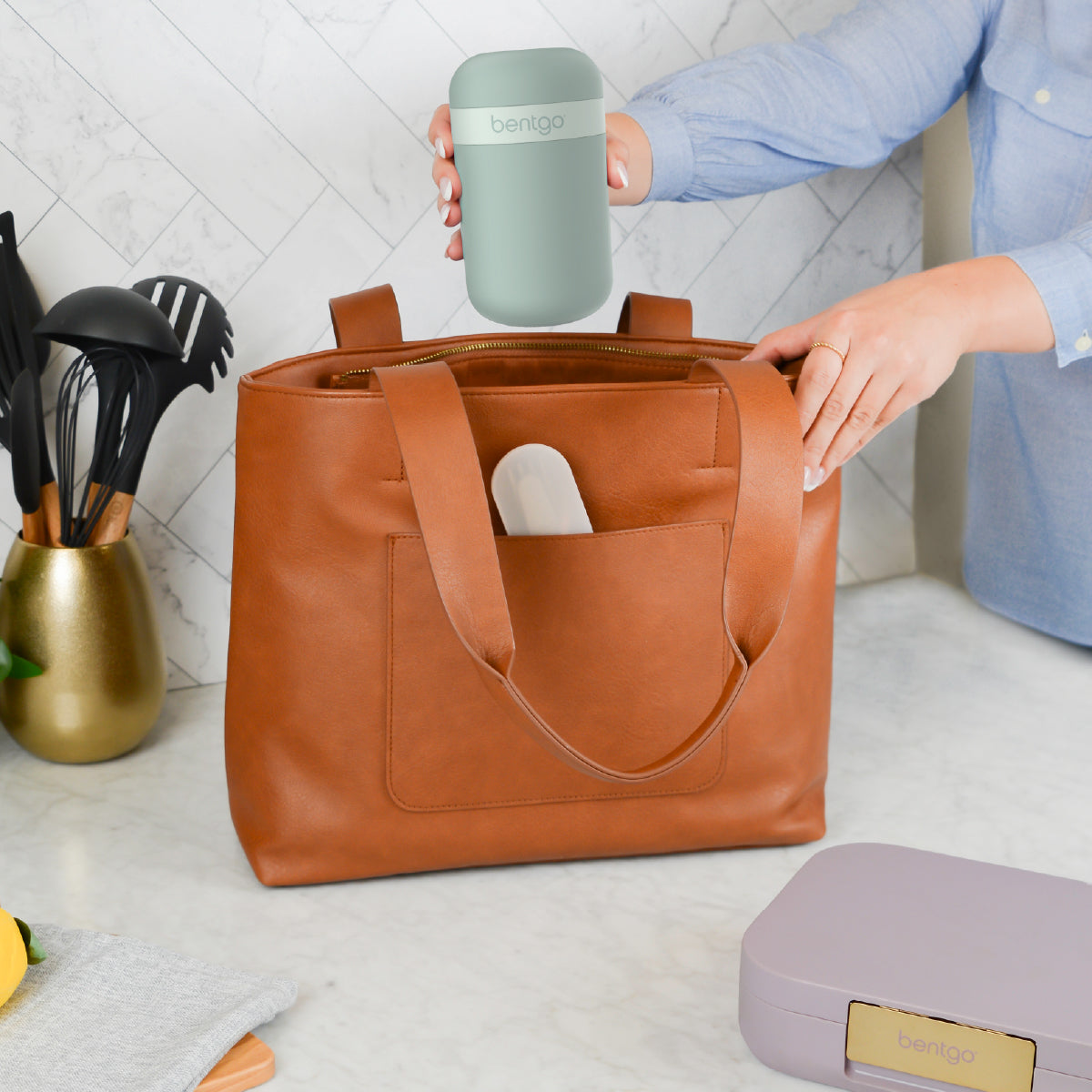 Person holding a green mug above a brown leather bag with a white interior pocket.