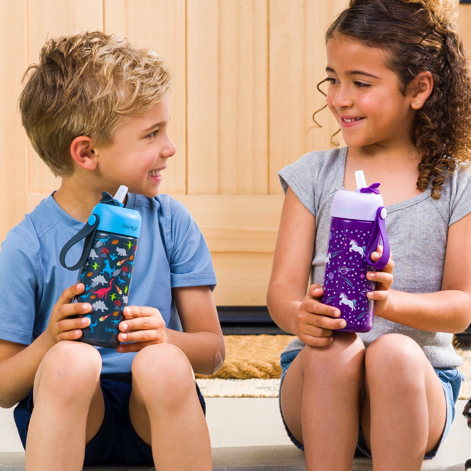 Two children holding colorful water bottles with animal prints.