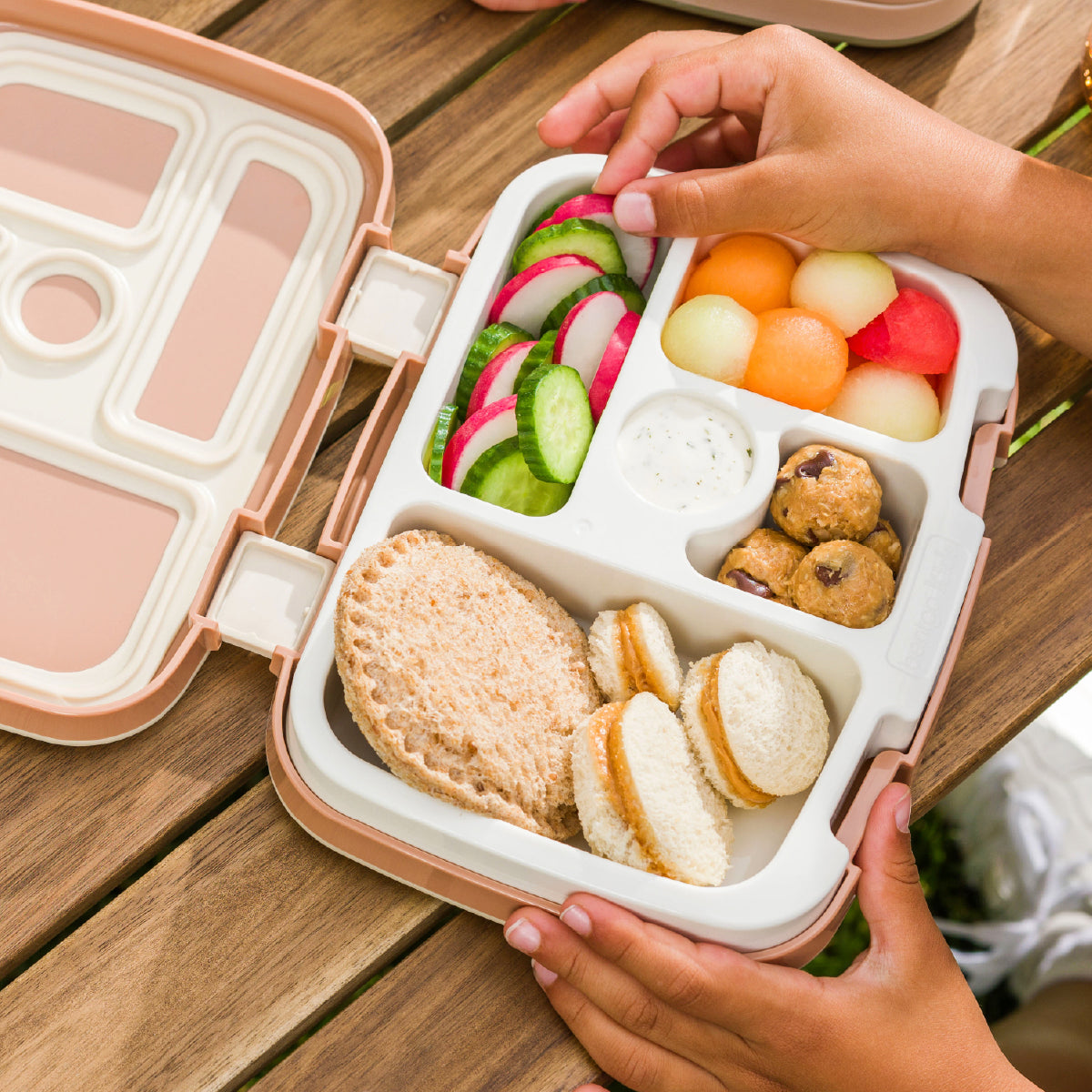 Person holding a bento box with various food items on a wooden table