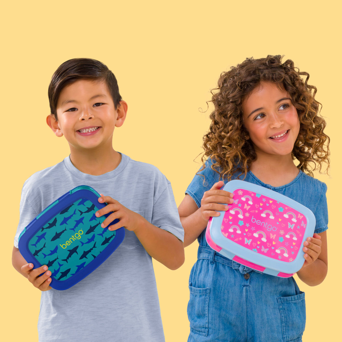 Two children holding lunch boxes with a yellow background